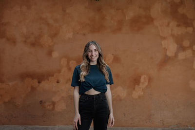 Portrait of smiling young woman standing against wall