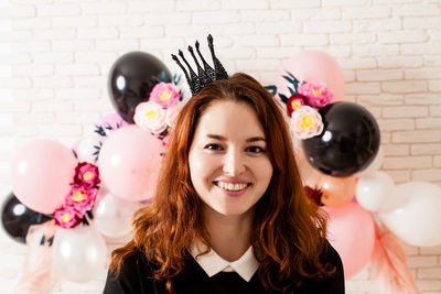 Portrait of smiling young woman with balloons against wall