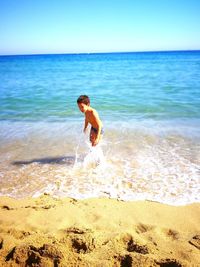 Shirtless boy playing with water at seashore