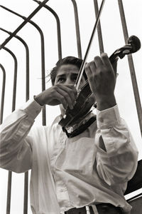 Low angle view of man playing violin against railing