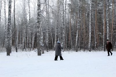 Full length of people walking on snow covered land in forest