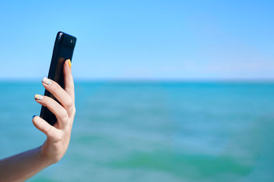 Midsection of man using mobile phone against blue sky