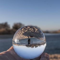 Close-up of hand holding crystal ball against clear sky