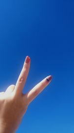 Cropped hand of woman against clear blue sky