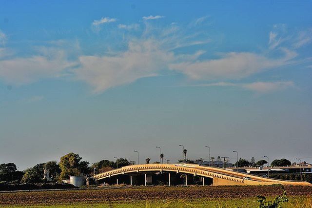 sky, transportation, built structure, architecture, connection, tree, bridge - man made structure, cloud - sky, incidental people, road, outdoors, blue, nature, day, landscape, cloud, tranquility, building exterior, no people, the way forward