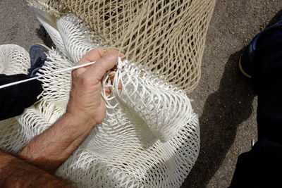 Cropped image of fisherman repairing fishing net on field