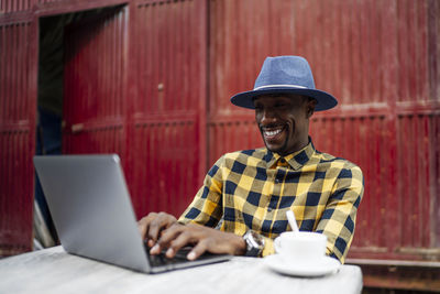 Smiling man using laptop at table against red metallic structure