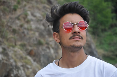 A north indian guy wearing white tshirt and red sunglasses with looking sideways 