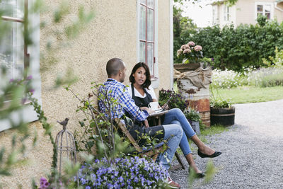 Owner discussing with male colleague over digital tablet while sitting outside cafe