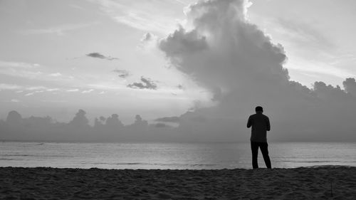 Man standing on shore at beach against sky