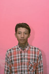 Portrait of young man standing against pink background