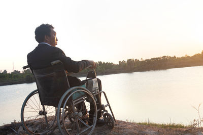 Side view of man sitting by lake against sky
