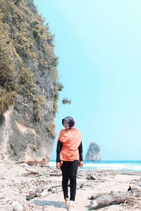 Rear view of man standing on shore against clear sky