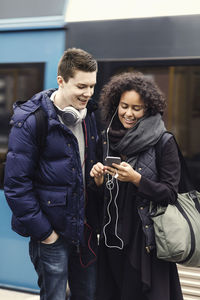 Multi-ethnic couple listening music through mobile phone on subway platform