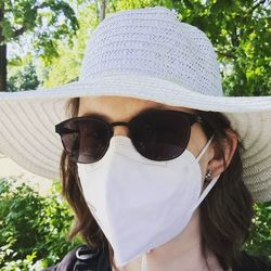 Portrait of woman wearing hat, sunglasses and face mask ffp2 / kn95 on a sunny day outdoors 