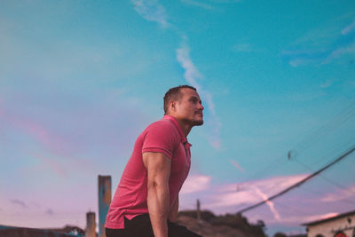 Side view of young man standing against blue sky