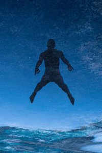 Silhouette man jumping in sea against blue sky