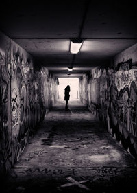 Silhouette woman standing in tunnel along graffiti walls