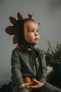 Toddler baby girl in funny dino costume sitting with eggs in hands