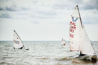Sailboats competition in sea against cloudy sky