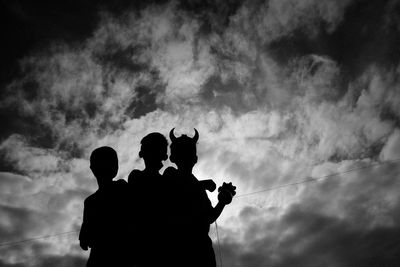 Low angle view of friends standing against cloudy sky