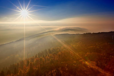 Sunlight streaming through clouds over landscape during sunset