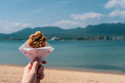 Midsection of person holding ice cream against sky