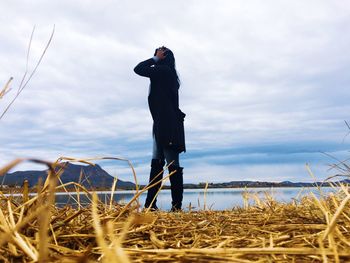 Side view of woman standing by sea against cloudy sky