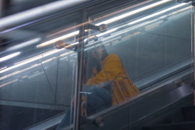 Young woman seen through glass sitting on escalator