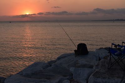 Fishing rod on rock by sea against sky during sunset