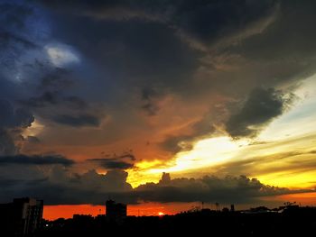 Silhouette buildings against dramatic sky during sunset