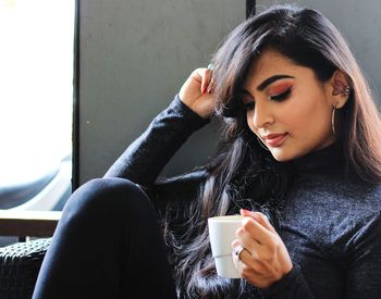 Young woman having coffee while sitting on sofa