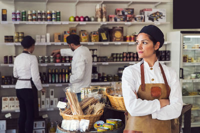 Thoughtful owner standing arms crossed while colleagues working in grocery store