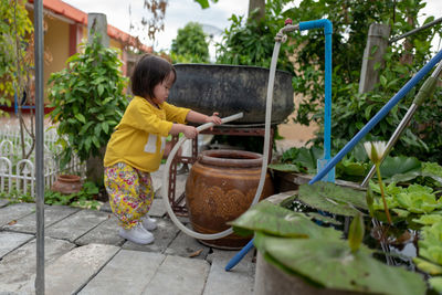 Side view of cute baby girl holding garden house while standing in yard