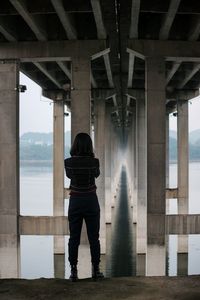 Rear view full length of woman standing below pier at beach