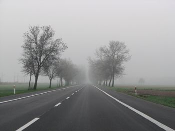 Empty road by trees against sky