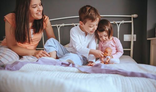 Cheerful mother playing with son and daughter while lying bed at home