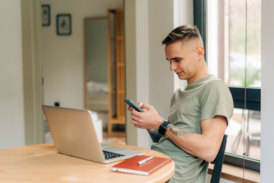 Man working from home using his laptop and mobile phone while sitting at a table in the living room