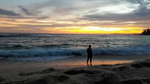 Woman standing on beach against sky during sunset