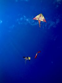 Low angle view of kites flying against blue sky