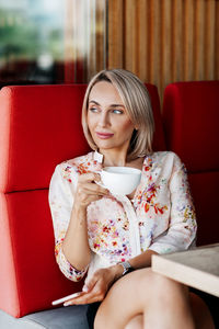 A beautiful girl is drinking coffee in a cafe and looking thoughtfully into the distance