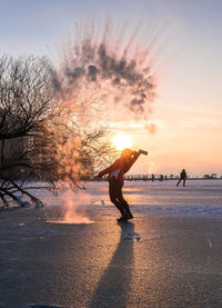 Silhouette man on bare tree against sky during sunset