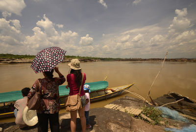 Rear view of people standing by lake on rock against sky