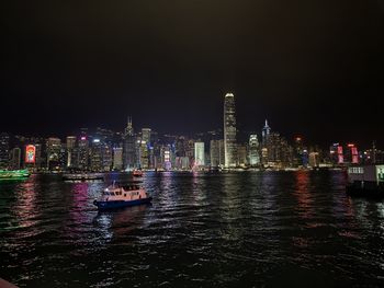 Illuminated buildings by river against sky at night