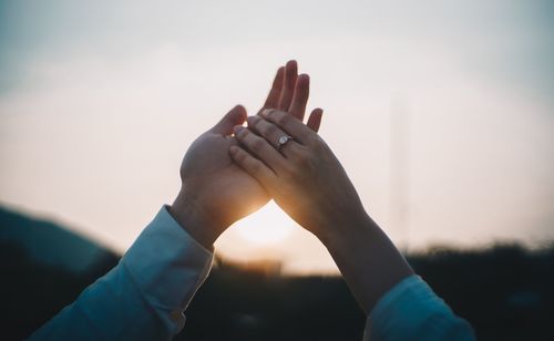 Close-up of hand against sky during sunset