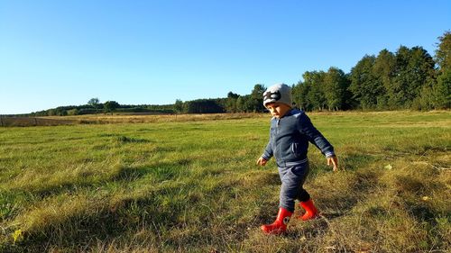 Boy walking on field against clear sky