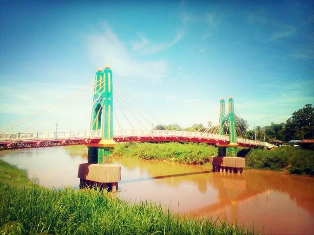 water, architecture, built structure, sky, connection, bridge - man made structure, river, grass, blue, cloud - sky, waterfront, reflection, building exterior, engineering, lake, nature, cloud, plant, green color, no people