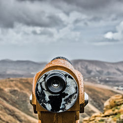 Close-up of weathered coin-operated binoculars against sky