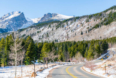 Road amidst trees and mountains against clear sky