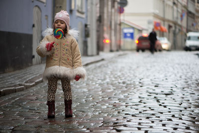 Girl eating lollipop while standing on street in city